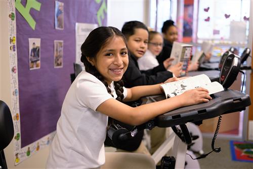 Student reading a book on an exercise bike desk 